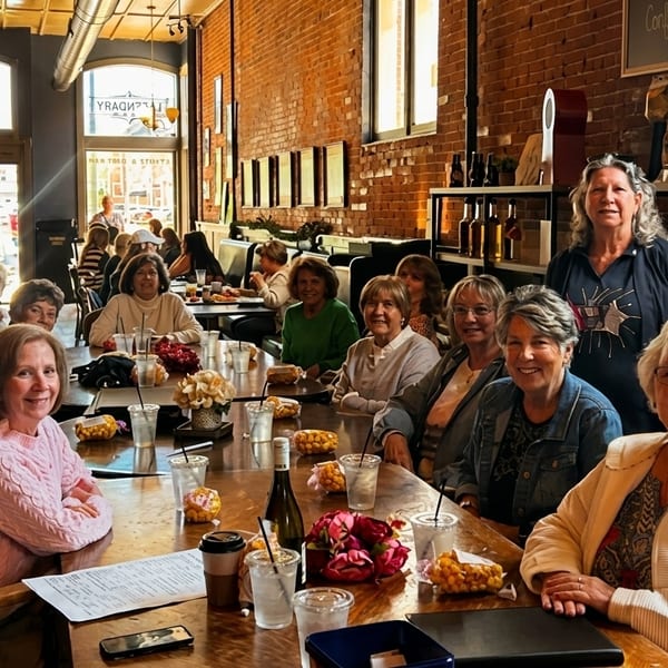 A group of women smiling and sitting at a long wooden table in a rustic restaurant.