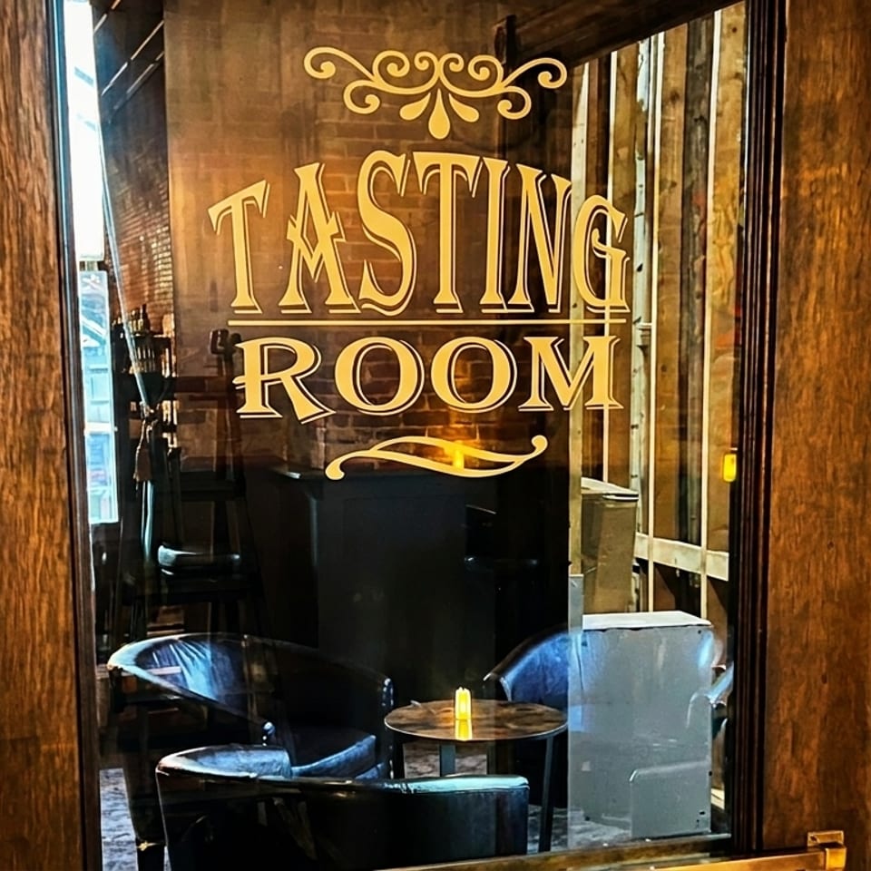 Glass door with "Tasting Room" in gold lettering, revealing a cozy interior with chairs and a table.