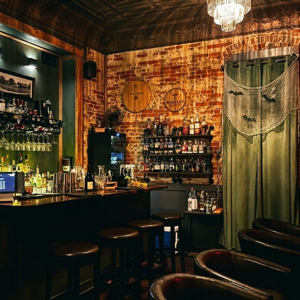 A dimly lit bar with a fully stocked liquor shelf, brick walls, and Halloween decorations.