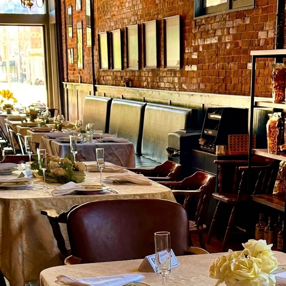 Elegant restaurant dining room with set tables, brick walls, and shelves of packaged goods.