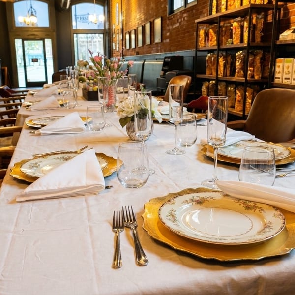 Long dining table set with elegant plates, silverware, and glasses in a restaurant.