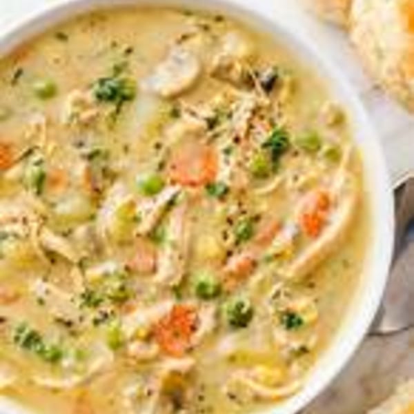 Creamy chicken pot pie soup with carrots, peas, and mushrooms, garnished with parsley.
