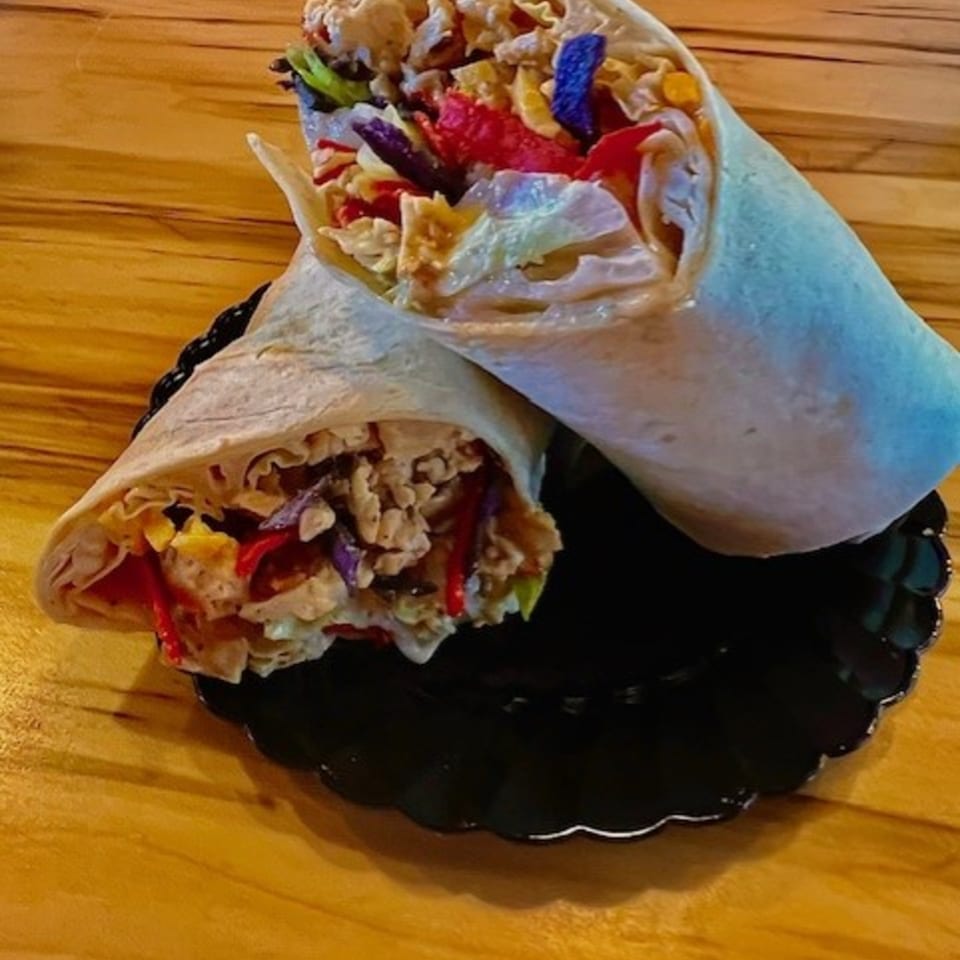 Two colorful wraps filled with chicken, red peppers, and purple cabbage on a black plate.