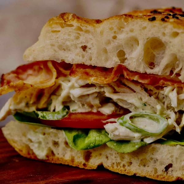 Close-up of a chicken salad sandwich with bacon, lettuce, and tomato on focaccia bread.