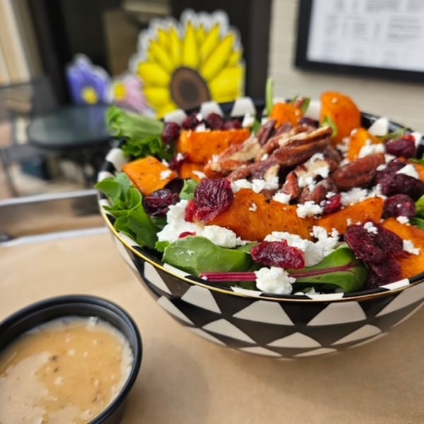 Sweet potato salad with pecans, cranberries, and feta cheese in a black and white bowl.