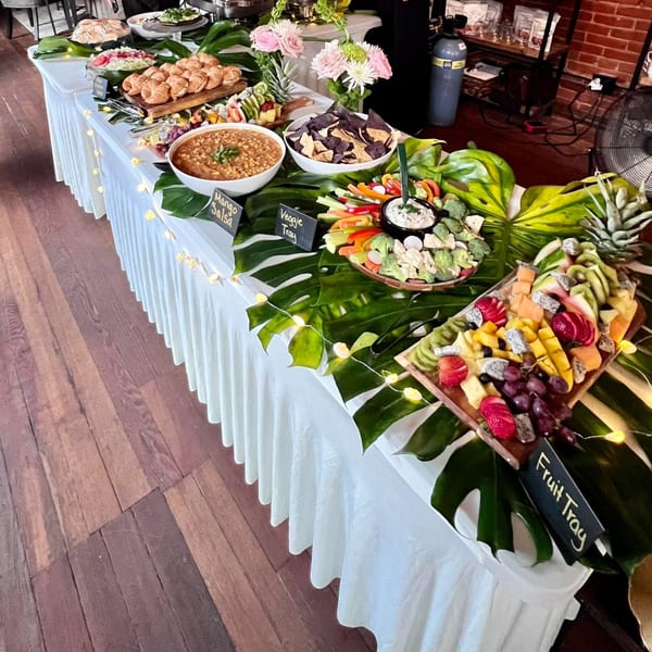 A buffet table with various appetizers including fruit, vegetables, salsa, chips, and croissants.
