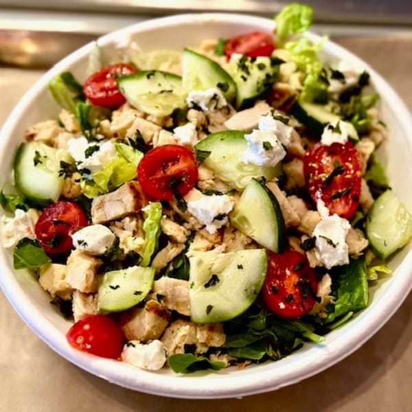 A vibrant salad with chicken, cherry tomatoes, cucumber, and feta cheese in a white bowl.