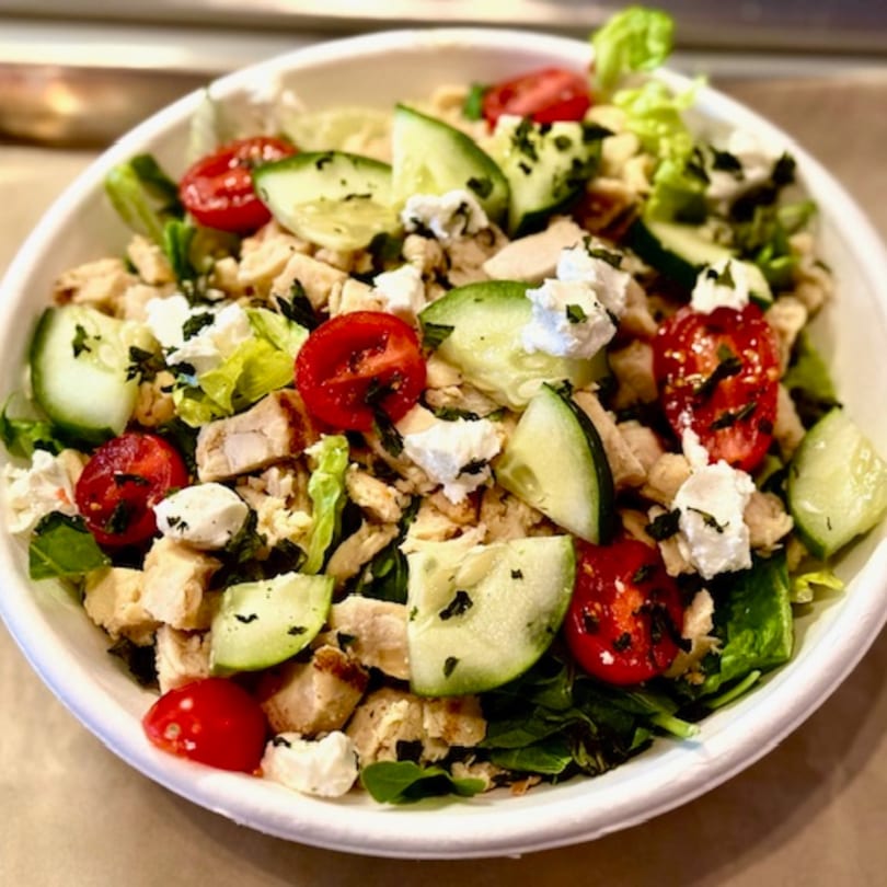 A vibrant salad with chicken, cherry tomatoes, cucumber, and feta cheese in a white bowl.