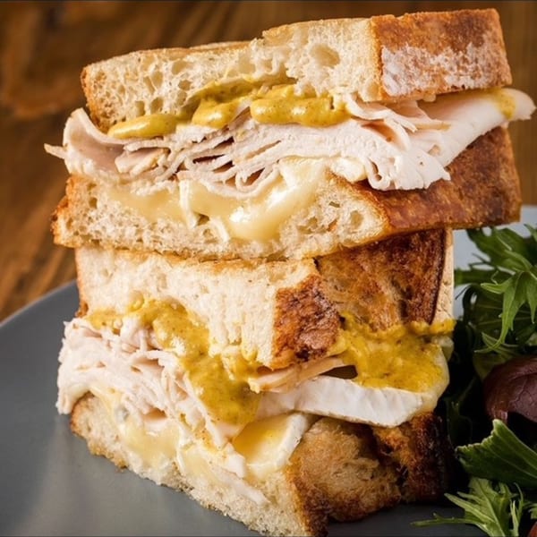 Two stacked turkey and cheese sandwiches with mustard drizzle, served with a side salad.