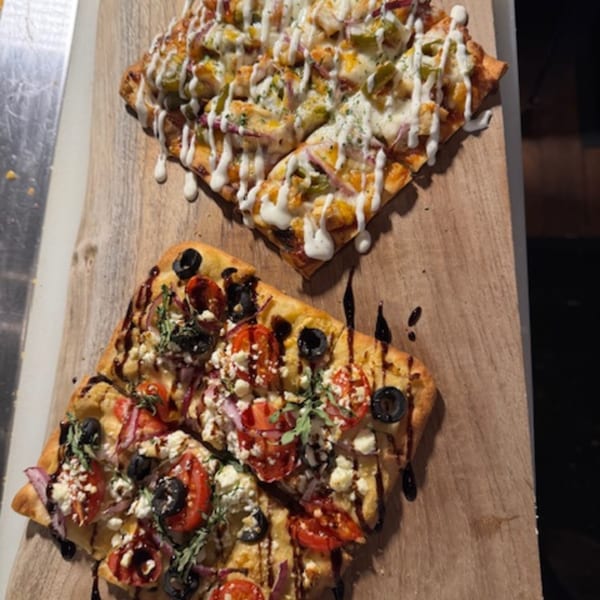 Two flatbread pizzas, one with white sauce and chicken, the other with tomatoes, olives, and feta.